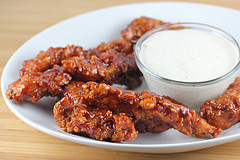 BBQ chicken strips coated in sauce served with ranch dressing on a white plate
