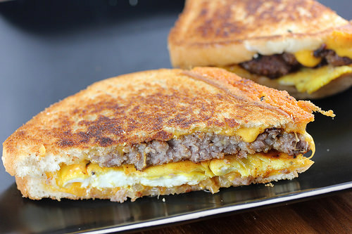Close-up of grilled breakfast patty melt layered with sausage, egg, and melted cheese