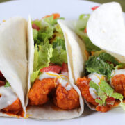 Buffalo chicken tacos topped with lettuce, tomato, and ranch dressing on a white plate