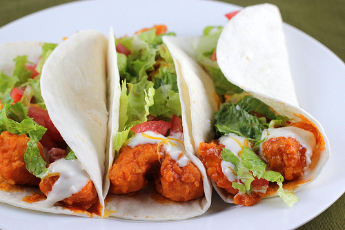 Buffalo chicken tacos topped with lettuce, tomato, and ranch dressing on a white plate