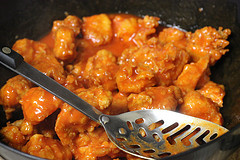 Crispy chicken pieces coated in buffalo sauce in a pan with a slotted spoon