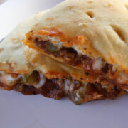 Cheesy calzone filled with meat and vegetables on a white plate