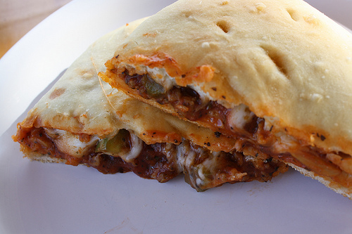 Cheesy calzone filled with meat and vegetables on a white plate