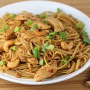 Bowl of chicken cashew noodles garnished with sliced green onions and chopsticks on the side