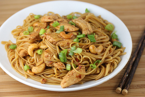 Bowl of chicken cashew noodles garnished with sliced green onions and chopsticks on the side