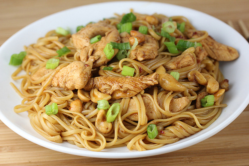 Chicken and cashew pasta topped with chopped green onions on a white plate