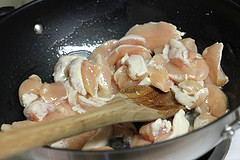 Raw chicken cooking in a wok stirred with a wooden spoon