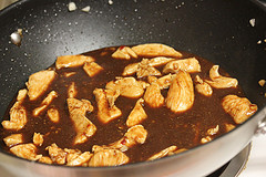 Chicken pieces simmering in brown sauce inside a wok