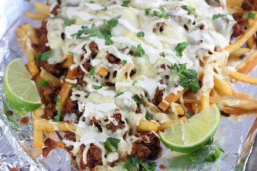 Loaded fries with chorizo, cheese, and lime wedges