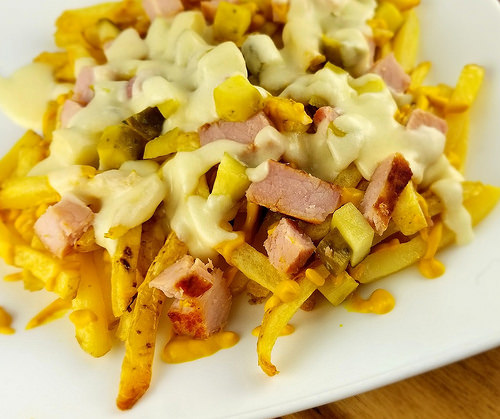 Close-up of Cuban fries loaded with ham, pickles, and melted cheese