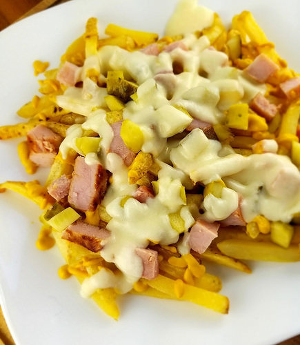 Cuban fries topped with diced ham, pickles, and melted cheese on a white plate
