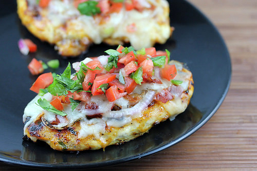 Grilled chicken breast topped with pico de gallo and melted cheese on a black plate