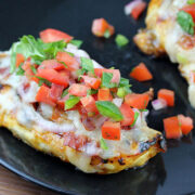 Grilled chicken breast topped with pico de gallo and melted cheese on a black plate
