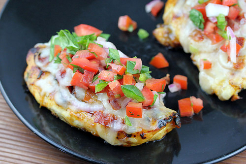 Grilled chicken breast topped with pico de gallo and melted cheese on a black plate