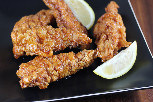 Honey pepper chicken strips with lemon slices on a black plate