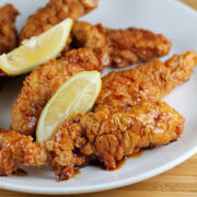 Honey pepper chicken strips with lemon wedges on a white plate