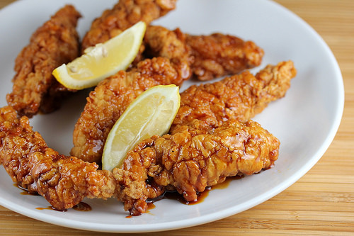 Honey pepper chicken strips with lemon wedges on a white plate