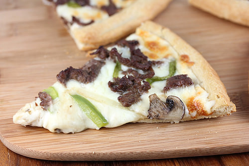 Slice of philly cheesesteak pizza with melted cheese and vegetables