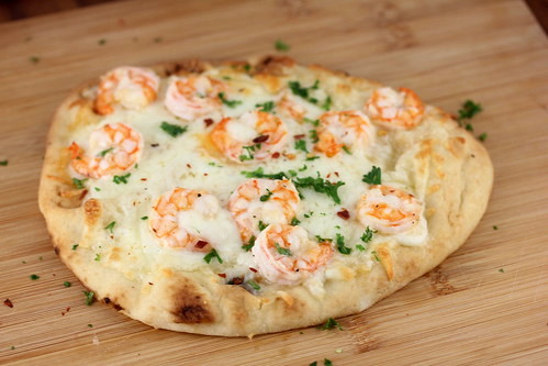 Whole shrimp scampi flatbread pizza with cheese and parsley on a wooden surface