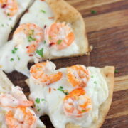 Sliced shrimp scampi flatbread topped with melted cheese and herbs on a wooden board
