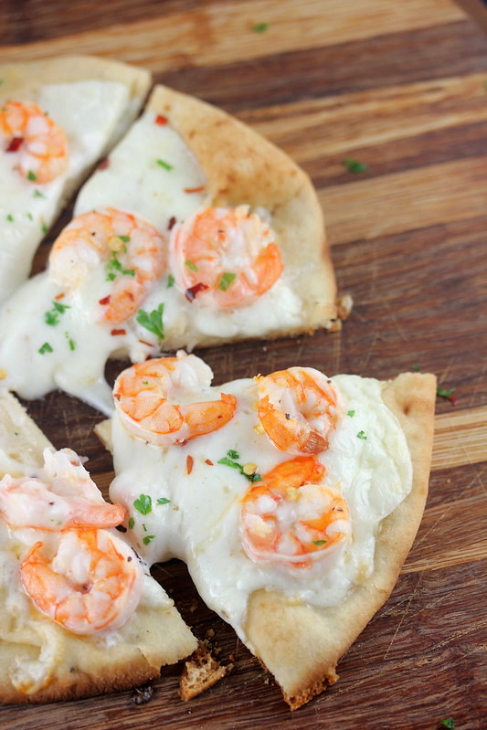 Sliced shrimp scampi flatbread topped with melted cheese and herbs on a wooden board