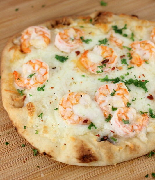 Close-up of shrimp scampi flatbread topped with melted mozzarella and fresh parsley