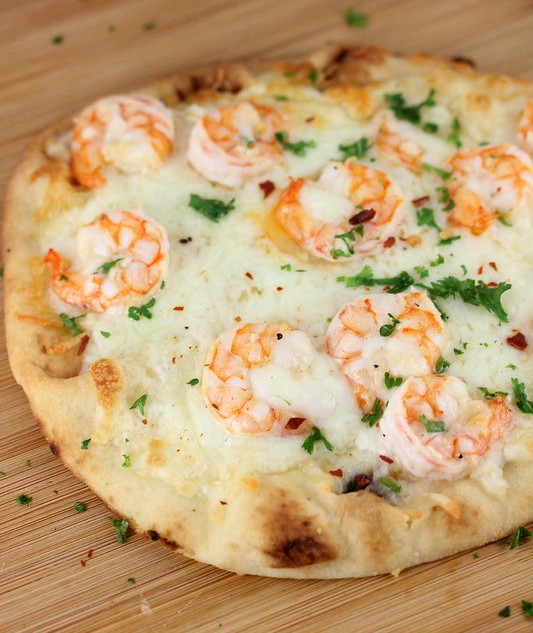 Close-up of shrimp scampi flatbread topped with melted mozzarella and fresh parsley