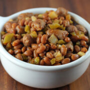 Close-up of spicy baked beans with sausage pieces and green peppers in a white bowl