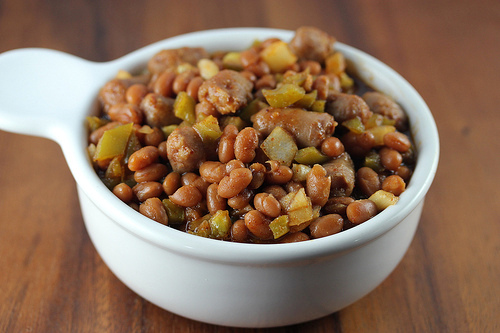Close-up of spicy baked beans with sausage pieces and green peppers in a white bowl