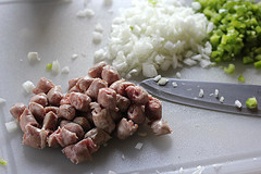Chopped sausage, onions, and green peppers on a cutting board with a knife