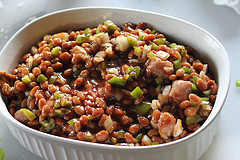 Unbaked spicy baked beans mixture with sausage, onions, and green peppers in a white dish