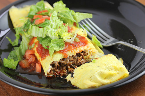 Taco omelet topped with salsa, lettuce, and diced tomatoes