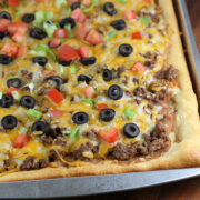 Taco pizza topped with ground beef, cheese, olives, tomatoes, and lettuce