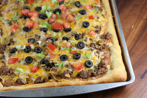 Taco pizza topped with ground beef, cheese, olives, tomatoes, and lettuce