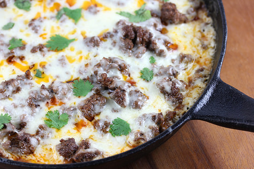 Skillet filled with cheesy ground beef tamale pie topped with cilantro