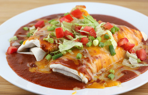 Plate of wet burritos topped with red sauce, melted cheese, lettuce, tomatoes, and green onions