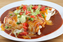 Enchilada-style burritos covered in sauce, cheese, lettuce, and diced tomatoes