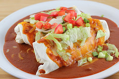 Smothered burrito topped with melted cheese, lettuce, tomatoes, and green onions