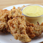 Close up of crispy chicken tenders next to sauce