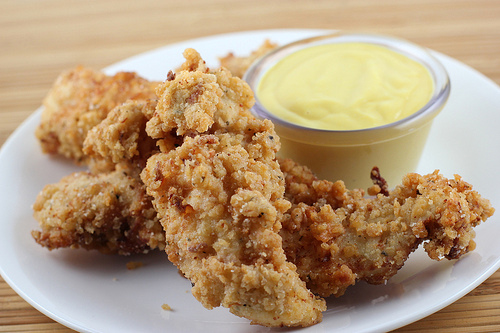 Close up of crispy chicken tenders next to sauce