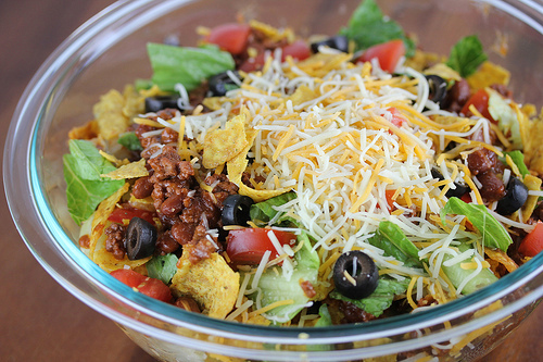 Taco salad in a bowl topped with shredded cheese, olives, and tomatoes