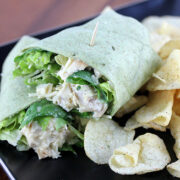 Spinach tortilla wrap filled with chicken Caesar salad served with potato chips