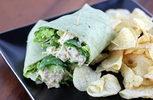 Spinach tortilla wrap filled with chicken Caesar salad served with potato chips