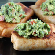 Plate of three golden chimichangas with guacamole on top
