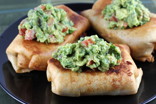 Plate of three golden chimichangas with guacamole on top