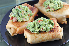 Fried chimichangas topped with guacamole on a dark plate