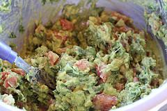 Chunky guacamole with tomatoes and herbs in a mixing bowl