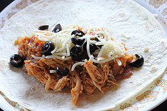 Shredded chicken, olives, and cheese placed on a flour tortilla