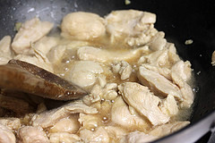 Chicken cooking in a pan with sauce being stirred