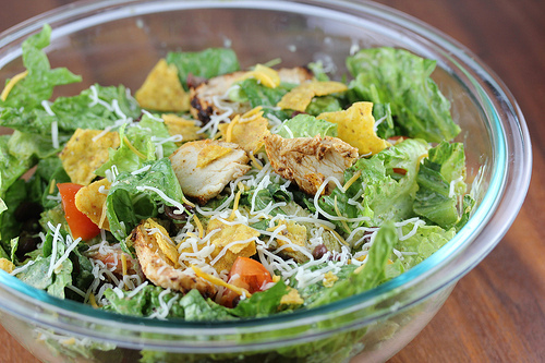 Chicken taco salad with shredded cheese, lettuce, tomatoes, and tortilla chips in a bowl